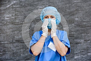 Medical nurse in potective uniform posing for camera. She`s wearing blue mask, hat and shirt