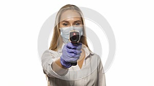 Medical nurse in protective mask pointing sensor thermometer on camera wearing white medical hospital robe. Young blond