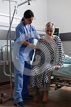 Medical nurse in scrubs helping senior woman in hospital room