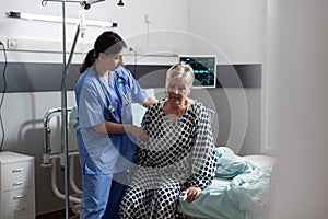 Medical nurse with stethoscope dressed in scrubs helping senior woman