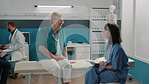 Medical nurse taking notes at consultation with elder patient