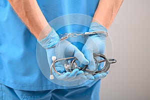 A medical officer, doctor, or quack in a blue medical uniform in handcuffs. The concept of crimes committed by medical personnel photo