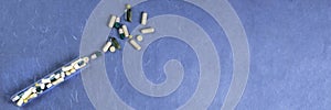 Medical pills, capsules, tablets spilling out from bottle on blue background