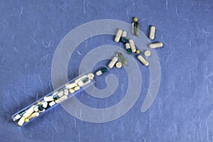 Medical pills, capsules, tablets spilling out from bottle on blue background