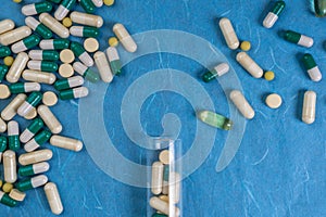 Medical pills, capsules, tablets spilling out from bottle on blue background