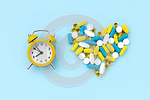 Medical pills in heart shape with alarm clock on blue background