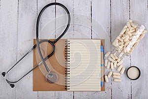 Medical pills, stethoscope and notebook on the table. View of a pharmacist doctor`s desk.