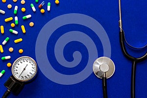 Medical pills, tonometer and stethoscope on the blue surface. Blood pressure measurement. Color capsules medication. Blue