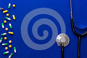 Medical pills, tonometer and stethoscope on the blue surface. Blood pressure measurement. Color capsules medication. Blue