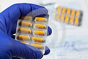 Medical practitioner wearing blue surgical latex gloves holding yellow drugs packet