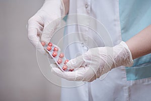 Medical practitioner wearing surgical latex gloves holding medicine bottle,taking out several white pills,COVID-19 corona virus