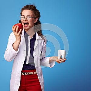 Medical practitioner woman with tooth biting an apple on blue