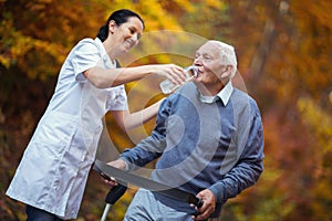 Medical professional helping a senior man with walker drink a wather