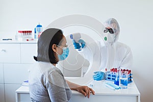 Medical professional in protective clothing measuring contactless fever at Covid-19 test center during coronavirus