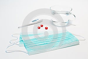 Medical protective face mask, three red tablets, electronic thermometer for measuring body temperature on a white background.
