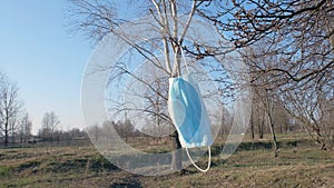 A medical protective mask hangs on a tree branch in the park. Health care and medicine concept