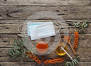 Medical protective mask with sea buckthorn branches, with berries, tea, honey and jam on a wooden background.The idea of