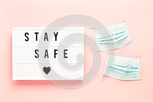 Medical protective mask and STAY SAFE written in light box on pink background. Healthcare and medical concept. Top view, copy