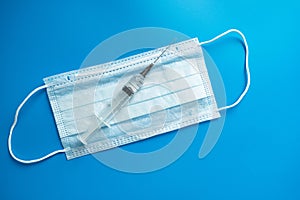 Medical protective mask syringe on a blue background. A typical 3-layer surgical mask for covering the mouth and nose.