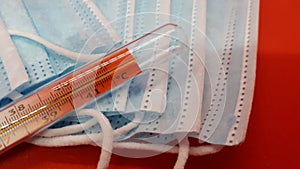 Medical protective masks and mercury thermometer on a red background