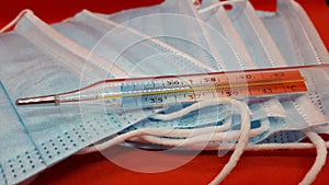 Medical protective masks and mercury thermometer on a red background