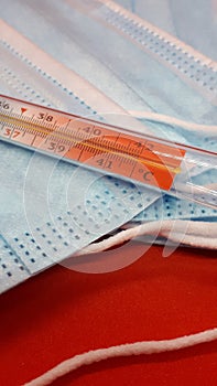 Medical protective masks and mercury thermometer on a red background