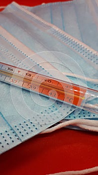 Medical protective masks and mercury thermometer on a red background