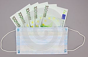 Medical protective surgical blue mask lies on money 100 euro banknotes on a gray background. Selective focus. Price increase for