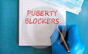 Medical and puberty blockers symbol. Words `puberty blockers` on white card. Doctor hand in blue glove and metallic pen. Beautif