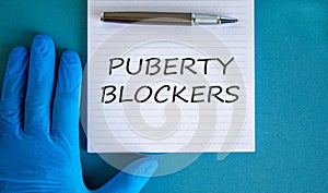 Medical and puberty blockers symbol. Words `puberty blockers` on white card. Doctor hand in blue glove and metallic pen. Beautif