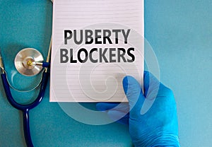 Medical and puberty blockers symbol. Words `puberty blockers` on white note. Doctor hand in blue glove and stethoscope. Beautifu