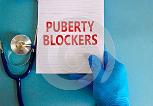 Medical and puberty blockers symbol. Words `puberty blockers` on white note. Doctor hand in blue glove and stethoscope. Beautifu