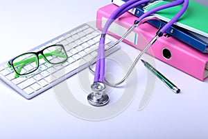 Medical record concept with stethoscope over pile of folders. Keyboard, glasses, pen, RX prescription. Selective focus