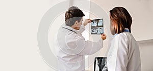 In medical room two young doctors radiologists analyzing x-ray and computer tomography film and discuss the xray diagnostic
