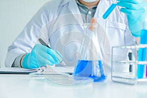 Medical science or male Compiling an Analysis Report in laboratory room research performs tests with blue liquid on test tube, photo