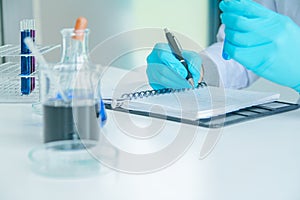 Medical science or male Compiling an Analysis Report in laboratory room research performs tests with blue liquid on test tube,