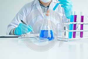 Medical science or male Compiling an Analysis Report in laboratory room research performs tests with blue liquid on test tube, photo