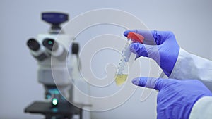 A medical scientist showing big test tube with vaccine liquid against the backdrop of laboratory equipment microscope