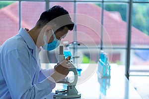 Medical scientist wearing protective surgical mask and lab gown using microscope in clinical laboratory