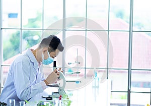 Medical scientist wearing protective surgical mask and lab gown using microscope in clinical laboratory