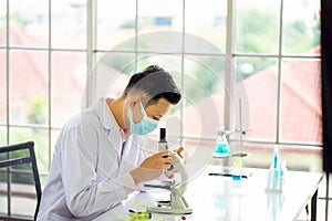 Medical scientist wearing protective surgical mask and lab gown using microscope in clinical laboratory