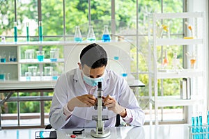 Medical scientist wearing protective surgical mask and lab gown using microscope in clinical laboratory