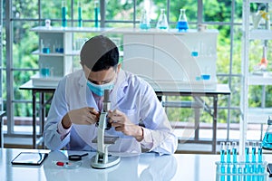 Medical scientist wearing protective surgical mask and lab gown using microscope in clinical laboratory