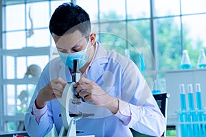 Medical scientist wearing protective surgical mask and lab gown using microscope in clinical laboratory