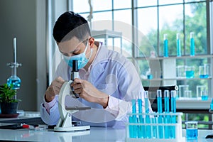 Medical scientist wearing protective surgical mask and lab gown using microscope in clinical laboratory