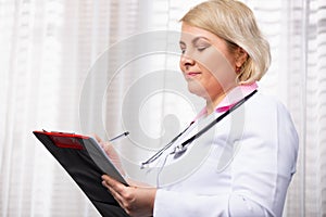 Medical services concept. Portrait of smiling female doctor writing in paper clipboard, taking patients history and smiling