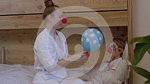 Medical sister with a red nose plays with a boy in his hospital ward