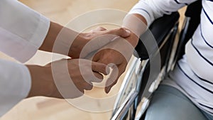 Medical social worker holding hand of disabled old patient.