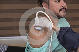 A medical sonographer using a transducer to conduct a shoulder ultrasound of a male patient at a clinic. Checking for any rotator