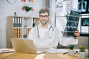 Medical specialist sitting at desk with x ray scan in hands